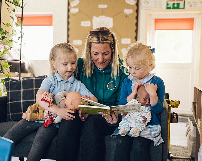 teacher sitting reading a book to 2 students